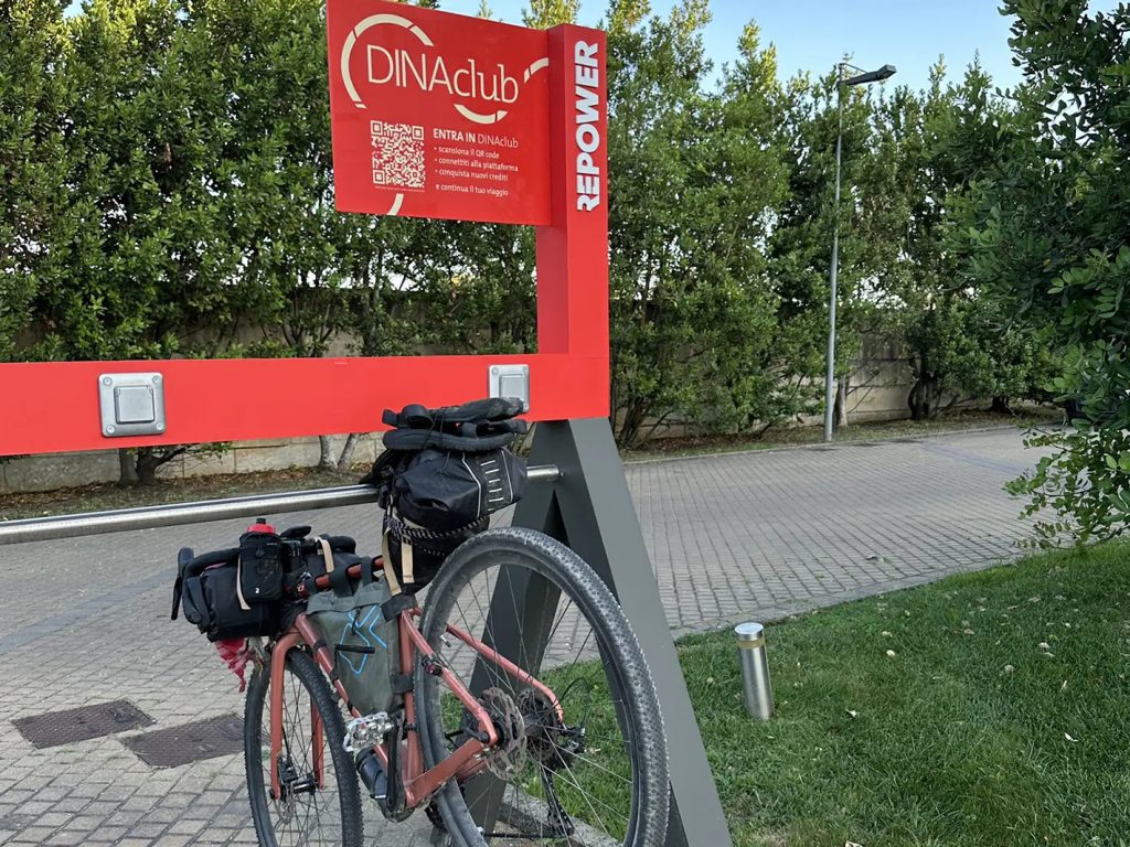 Bici gravel con borse parcheggiata alla rastrelliera rossa DINAclub Repower in Puglia