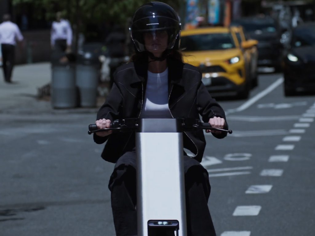 Persona con casco guida la e-bike Olto in una strada cittadina trafficata con un taxi giallo