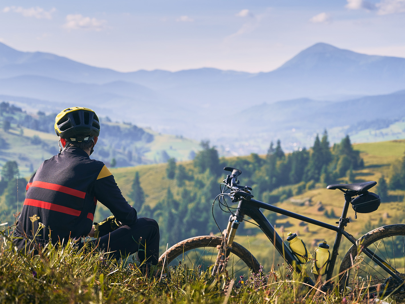 Ciclista con casco giallo riposa sul prato accanto alla bici osservando valli e montagne nebbiose