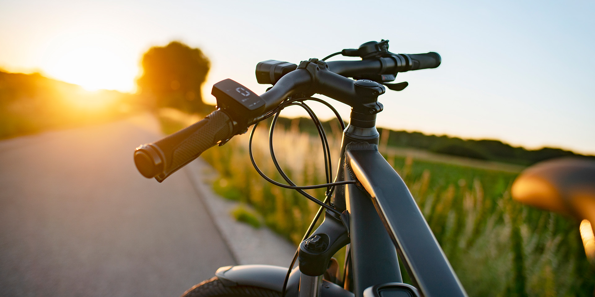 Dettaglio del manubrio di una e-bike con display e freni controluce su strada al tramonto